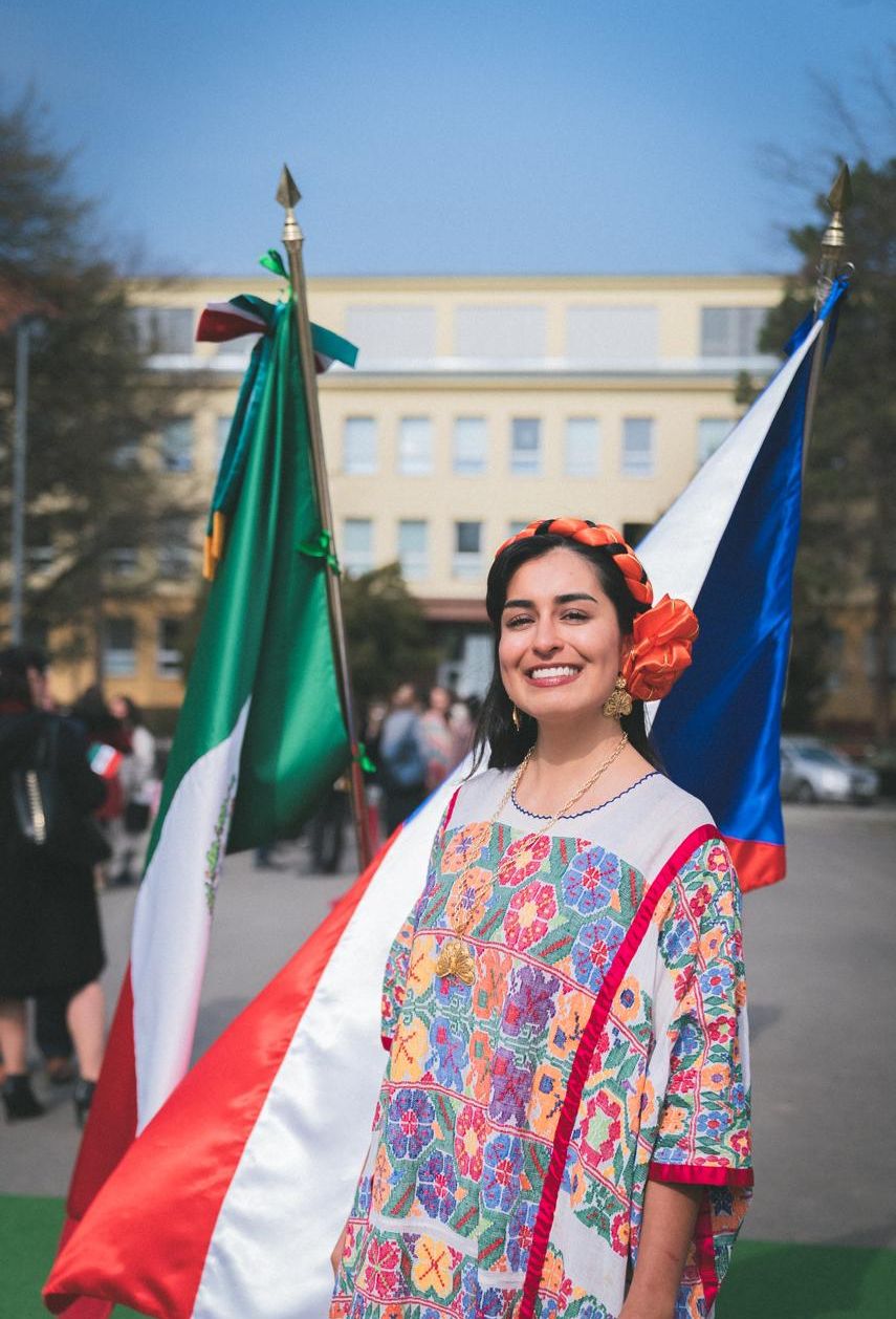 Naomi Luna con huipil oaxaqueño entre las banderas de México y la República Checa